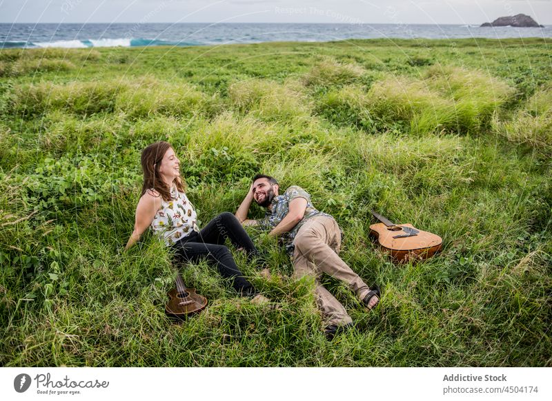 Musiker mit Gitarre und Ukulele im Gras am Meer liegend im Tageslicht Frau Mann Freund Instrument Natur Küste Gitarrenspieler männlich tagsüber spielen MEER