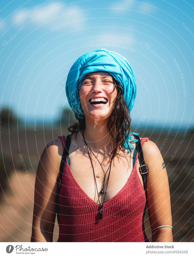 Fröhliche Frau mit Kopftuch steht in der Natur in sonnigen Tag positiv Lachen Landschaft Optimist heiter froh Glück Freude braune Haare lässig tagsüber charmant