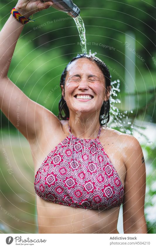 Fröhliche Frau gießt sich im Sommer Wasser auf den Kopf Flasche Park eingießen Baum Glück heiter nasses Haar Top Augen geschlossen Natur Lächeln Lachen Freude
