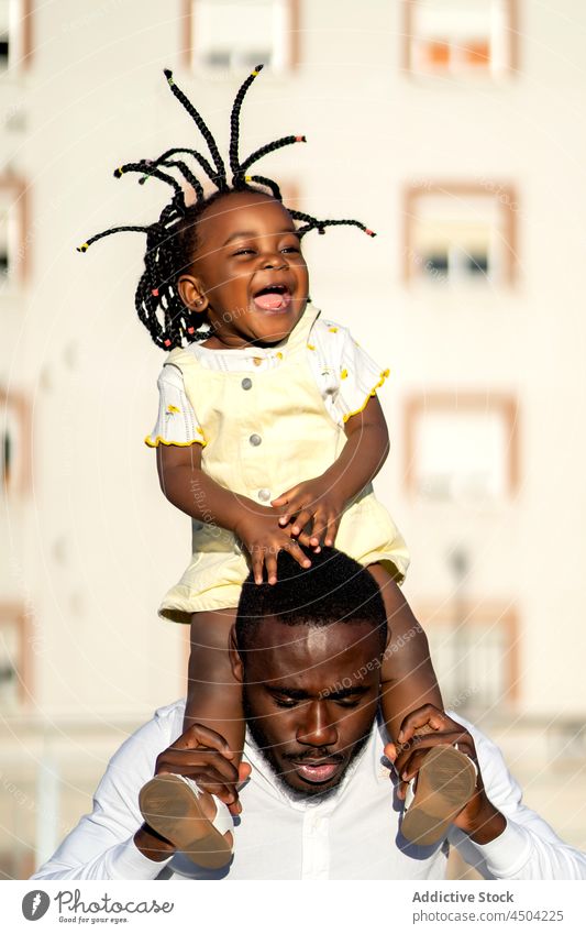 Glücklicher schwarzer Vater springt mit Tochter auf den Schultern auf der Straße Mann Mädchen Spaß Kind springen Vaterschaft Eltern heiter Frau Afroamerikaner