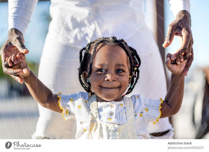 Lächelndes schwarzes Mädchen geht mit Vater auf der Straße Spaziergang Glück Kind positiv Freude Eltern Händchenhalten Papa Afroamerikaner Tochter Kindheit