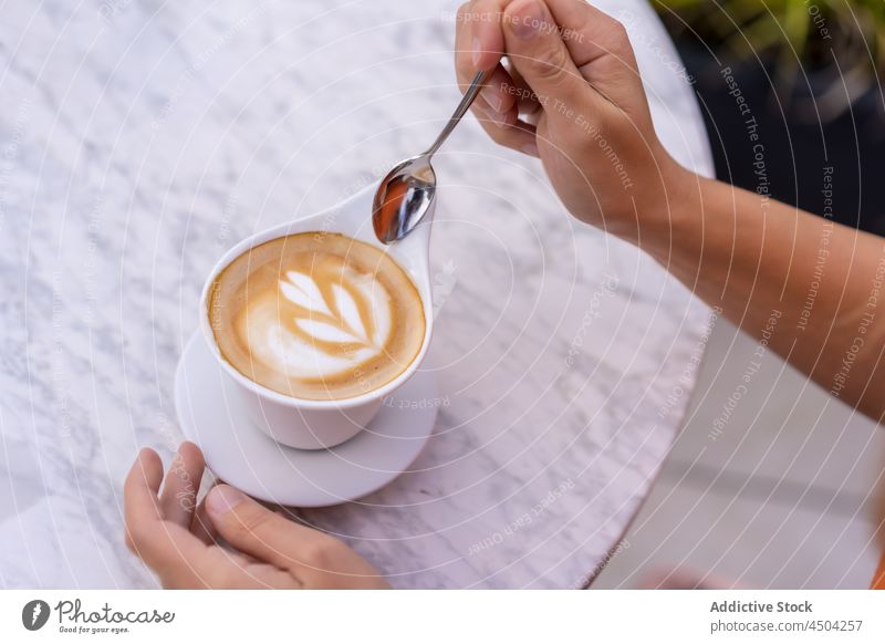 Crop Person hält Löffel über Tasse Latte Kaffee Latte Art Becher Getränk Heißgetränk Tisch geschmackvoll Koffein lecker aromatisch kreativ Design Kantine
