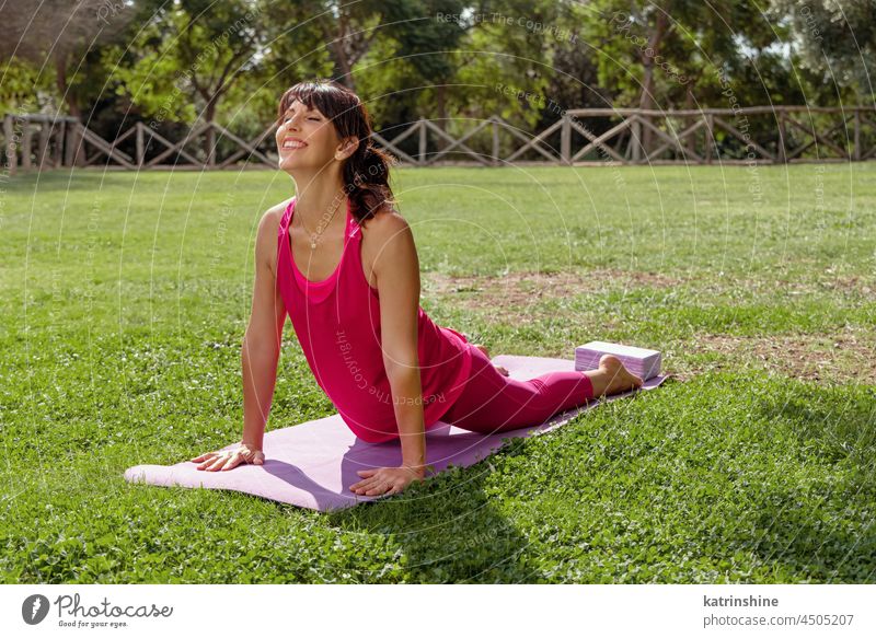 Frau übt Pilates-Pose Cobra im Park im Sommer Yoga Asana Gesundheit strecken rosa grün sonnig mittleres Alter Kobra im Freien Fitness Training Lifestyle Übung