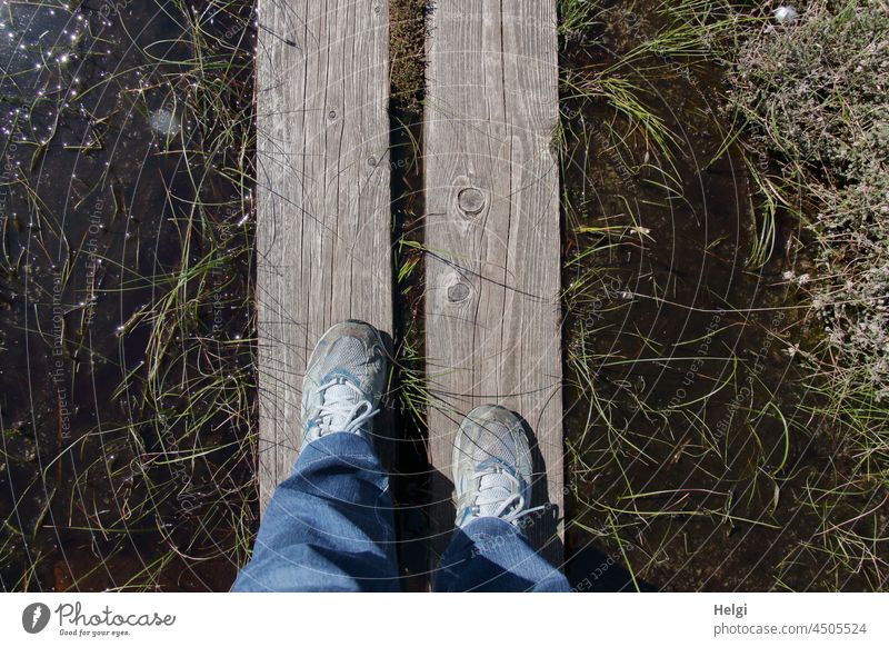 ein schmaler Weg - Füße der Fotografin auf einem Holzsteg im Moor, an den Seiten Wasser und Moorpflanzen Holzweg Holzstreg Moorweg Schuhe Hose Pflanzen