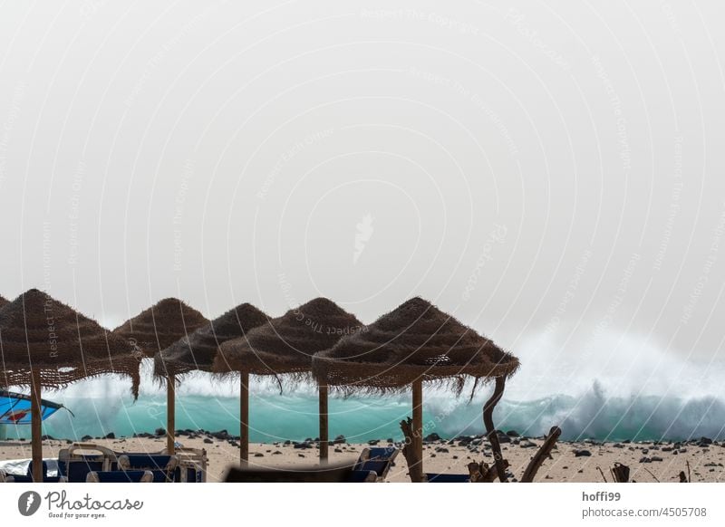 Sonnenschirme aus Naturfasern am Strand vor spritzender Gischt sommersehnsucht Strandbar Wellen Atlantik Atlantikküste Urlaub urlaubstimmung wegfahren Wärme
