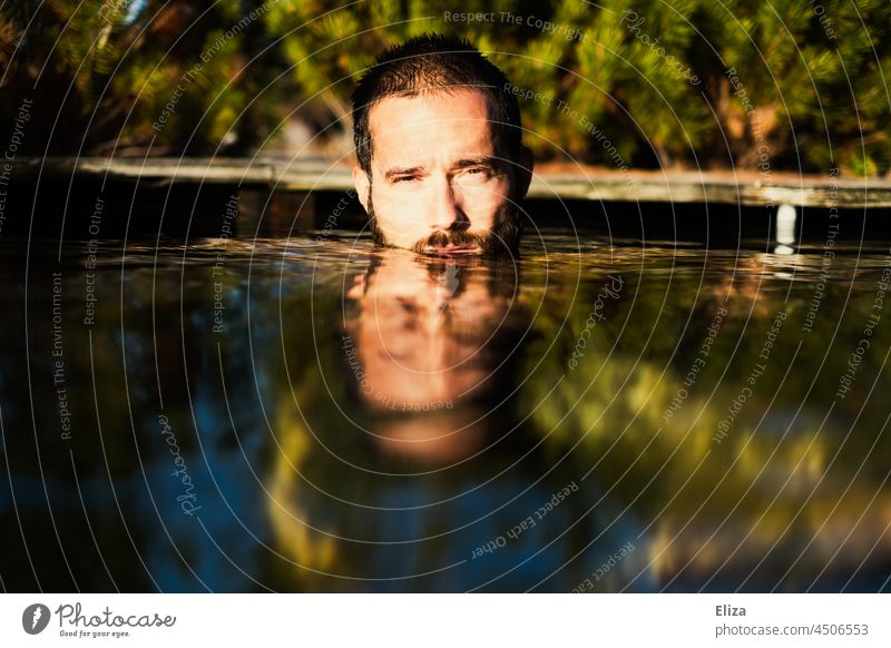Ein Mann, das Gesicht halb unter Wasser, badet draußen, umgeben vom Natur, bei Sonnenschein baden Sommer See Spiegelumg Portrait Mensch Wärme Sonnenlicht