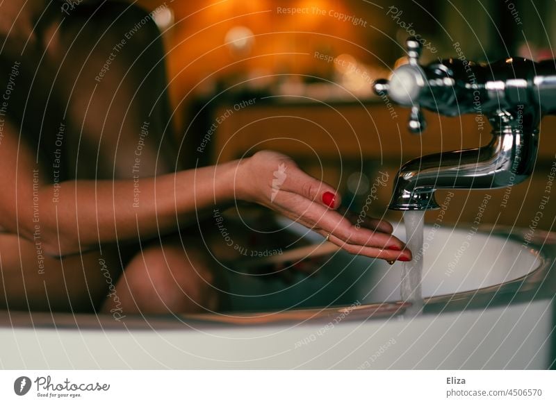 Eine Frau sitzt in der Badewanne und überprüft mit der Hand die Wassertemperatur baden ein Bad nehmen sitzen Körperpflege Wasserhahn Mensch
