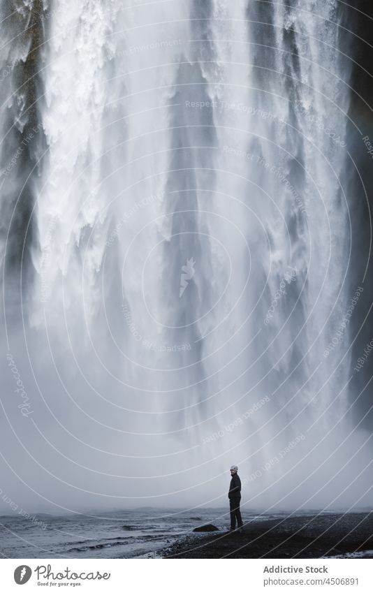 Männlicher Reisender steht unter einem malerischen Wasserfall Mann bewundern Fluss Natur Klippe Landschaft strömen spektakulär Wanderer männlich lässig felsig