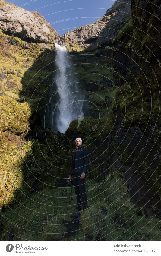 Junger ethnischer männlicher Fotograf bewundert die Natur in der Nähe eines Wasserfalls während einer Reise in Island Mann bewundern Schlucht Fotoapparat