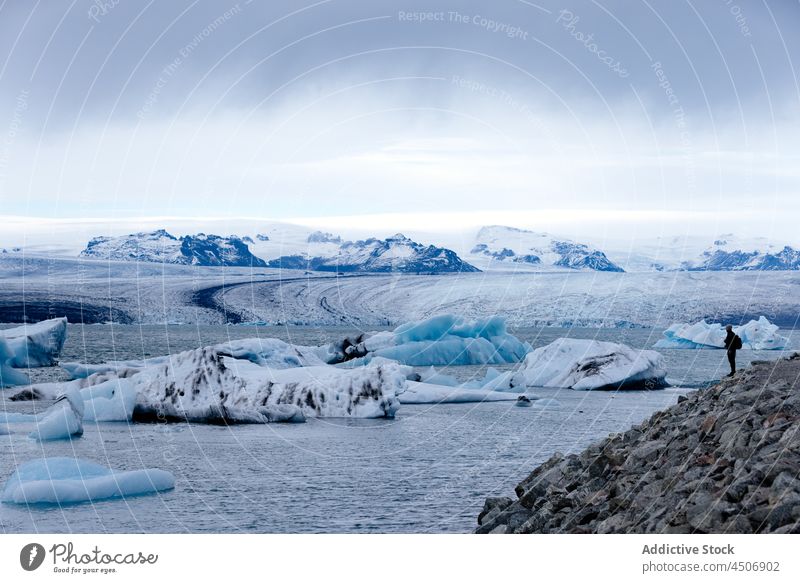 Unbekannter Forscher beobachtet Gletscher und kräuselnden See unter bewölktem Himmel Person bewundern Wanderer Landschaft Natur Winter erkunden Hochland