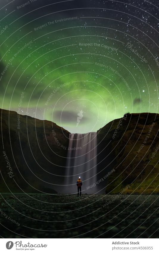 Anonymer Reisender, der den Sternenhimmel mit Polarlichtern in der Nähe eines malerischen Wasserfalls beobachtet Person bewundern Nacht polar Klippe Natur
