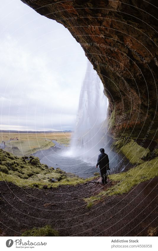Unbekannter Mann steht in der Nähe eines reißenden Wasserfalls, der durch eine Felswand fließt Klippe Höhle bewundern Natur Kraft Reisender erkunden Landschaft