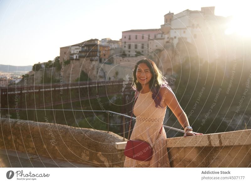 Fröhliche ethnische Frau im Kleid lehnt sich an eine Steingrenze Sonnenuntergang historisch Stadt Stadtbild Hügel anziehen Glück genießen Zaun Steg alt positiv