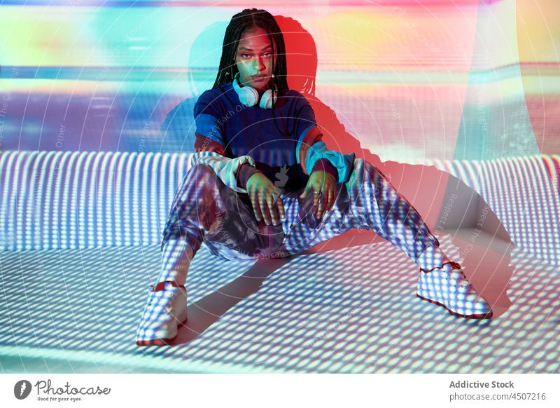 Stilvolle junge ethnische Dame schaut in die Kamera in einem beleuchteten Studio Frau selbstsicher Mode Vorschein cool kreativ Projektor Model Persönlichkeit