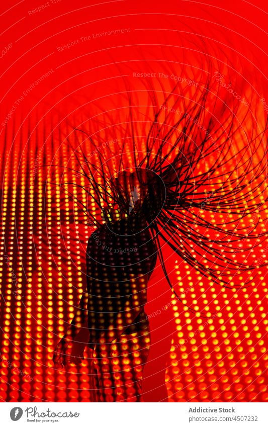 Anonyme ethnische Frau, die in einem Studio mit roten Lichtern tanzt Haare schütteln Tanzen trendy cool ausführen Nachtleben neonfarbig Stil sich[Akk] bewegen