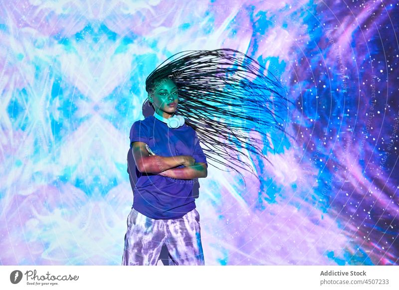Ethnische Frau tanzt in einem Studio mit blauen und lilafarbenen Lichtern Haare schütteln Tanzen trendy cool ausführen Nachtleben neonfarbig Stil