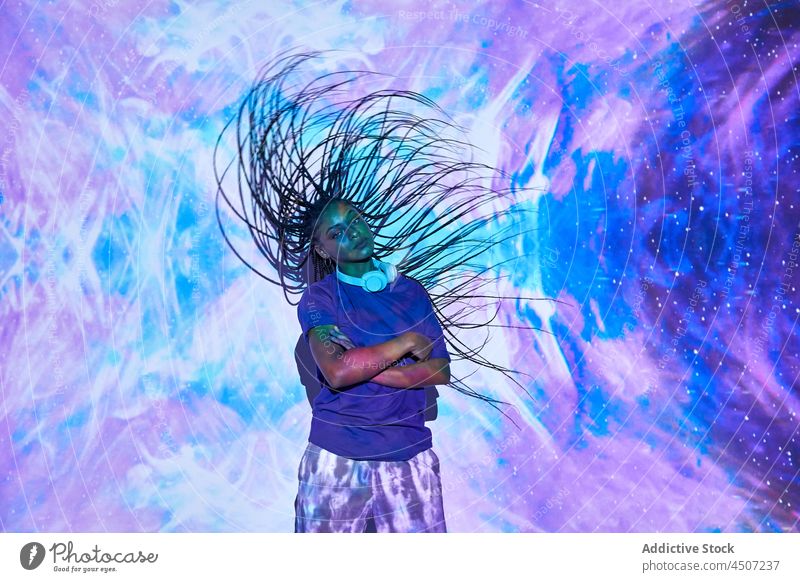 Ethnische Frau tanzt in einem Studio mit blauen und lilafarbenen Lichtern Haare schütteln Tanzen trendy cool ausführen Nachtleben neonfarbig Stil