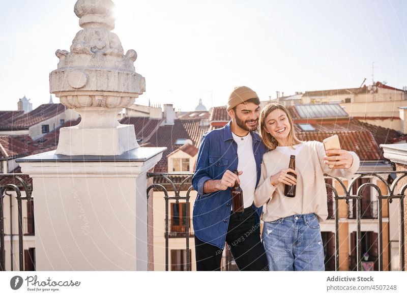 Lächelnde Freunde trinken Bier und machen ein Selfie Mann Frau benutzend Smartphone positiv teilen Balkon online männlich Glas Internet Funktelefon Alkohol