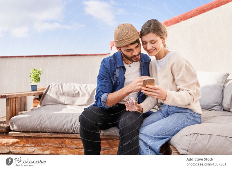Lächelndes Paar, das zusammen auf der Couch ein Smartphone benutzt zuschauen teilen benutzend Terrasse Anschluss online Internet Suche Mann Frau Freund Freundin