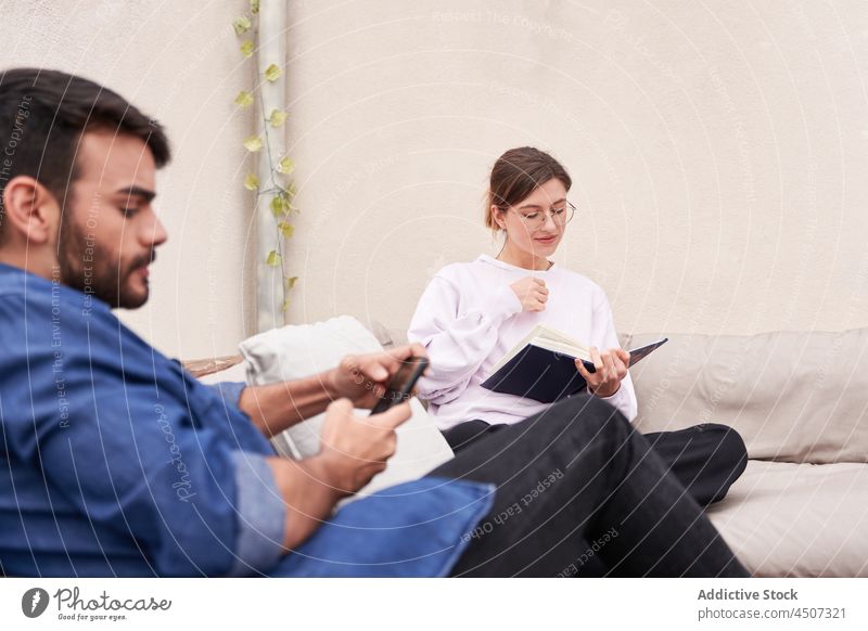Mann benutzt Smartphone in der Nähe einer Frau, die ein Buch liest lesen benutzend Freizeit Konzentration Zeitvertreib Hobby männlich Freund Surfen Browsen