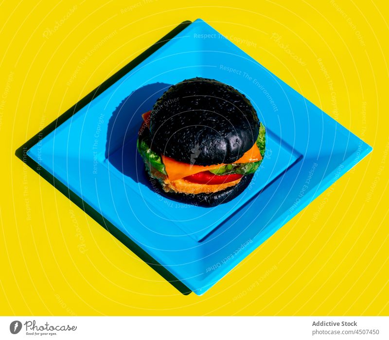 Schwarzer Burger auf quadratischem blauem Teller Junk Food farbenfroh hell Geometrie Speise Mittagessen Portion Design einfach sehr wenige Form Quadrat Fastfood