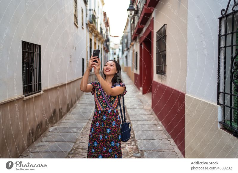 Fröhliche asiatische Frau beim Fotografieren in einer engen Straße Smartphone fotografieren einfangen Stadt Gebäude Tourist gealtert beobachten bewundern Moment