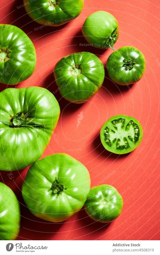 Grüne Tomaten verstreut auf leuchtend rotem Hintergrund grün unreif Ackerbau hell Streuung Scheibe Ernte Agronomie Bauernhof Solanum lycopersicum Vitamin