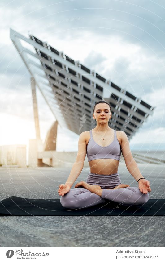Frau macht Lotus-Pose auf der Straße padmasana Yoga Asana solar Panel Übung Training üben Energie Dame modern Sportbekleidung Wellness Augen geschlossen