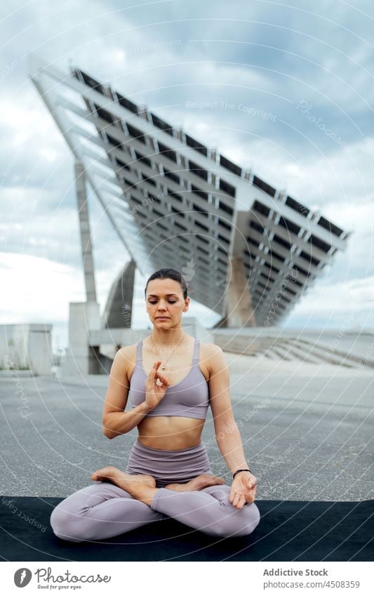Frau macht Lotus-Pose auf der Straße padmasana Yoga Asana solar Panel Übung Training üben Energie Dame modern Sportbekleidung Wellness Augen geschlossen