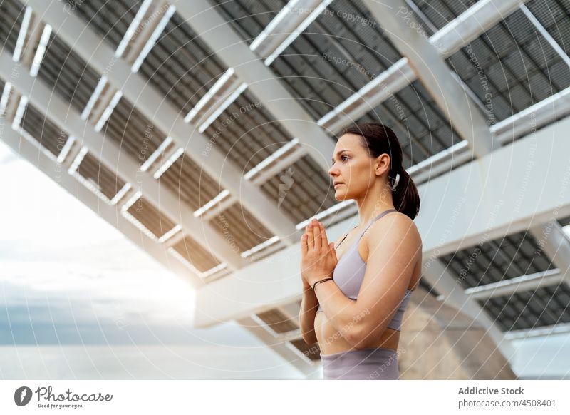 Friedliche Frau macht Namaste-Geste beim Training Yoga Asana gestikulieren solar Panel Übung Straße üben Energie Dame modern Sportbekleidung Wellness