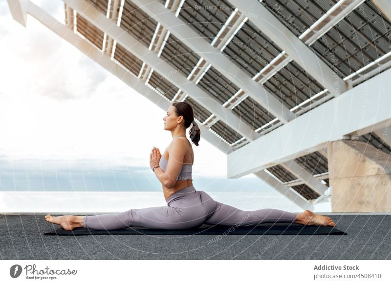 Flexible Frau in Hanumanasana-Haltung Yoga hanumanasana Spagat vorwärts beugen Asana solar Panel Übung Training Straße üben Energie beweglich Dame modern