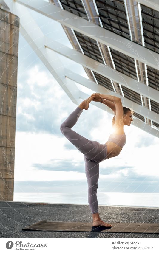 Flexible Frau übt Yoga-Asana in der Nähe eines Solarpanels solar Panel Stehende Teilung gebeugtes Knie Übung Training Straße üben Energie beweglich Dame