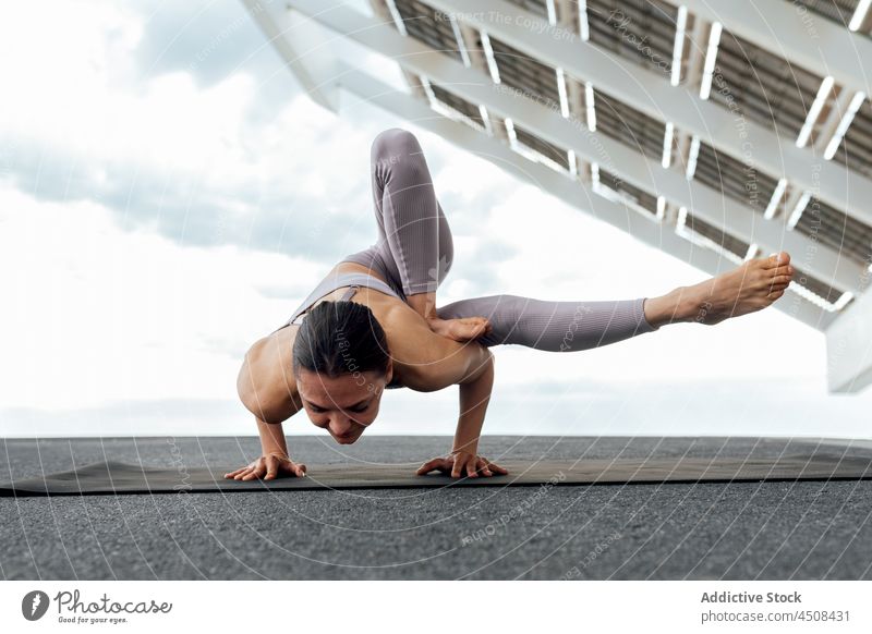 Flexible Frau beim Grashüpfer-Asana auf der Straße Yoga Heuschrecke maksikanagasana solar Panel Übung Training üben Energie beweglich Dame modern