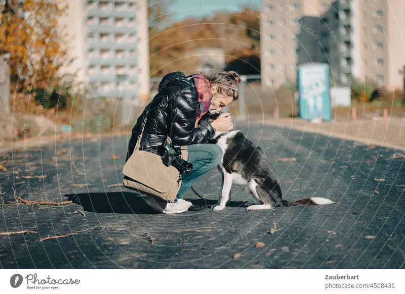 Ein glückliches Paar - Frau sitzt mit ihrem Hund auf der herbstlichen Straße Haustier Liebe Zuneigung Vertrauen Zweisamkeit Herbst Hochhäuser zusammengehörig