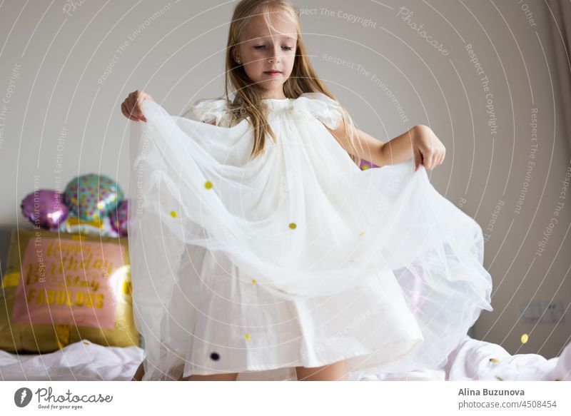 Cite kleinen kaukasischen Mädchen feiern acht Jahre alt Geburtstag zu Hause. Stylish Kid trägt modisches Kleid und haben Spaß mit Konfetti auf dem Bett
