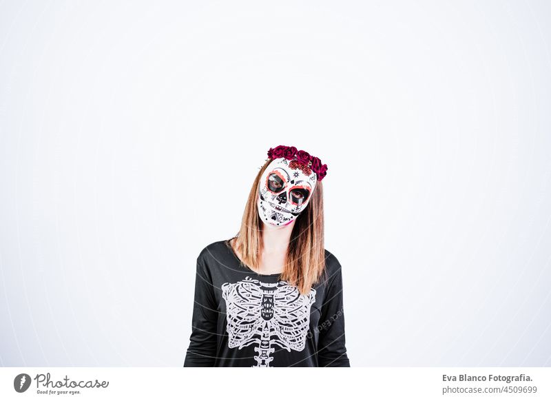 Frau trägt mexikanische Gesichtsmaske während Halloween-Feier. Skelett-Kostüm und rote Rosen Diadem auf dem Kopf. Frau macht Stille Geste mit dem Finger. Halloween-Party-Konzept