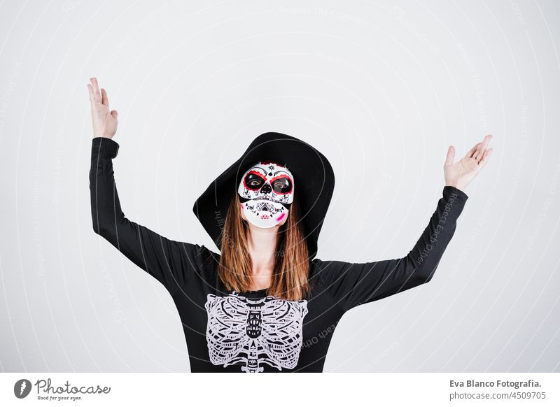 Frau trägt mexikanische Gesichtsmaske während Halloween-Feier. Skelett-Kostüm und schwarzen stilvollen Hut. Frau mit erhobenen Armen. Halloween-Party-Konzept