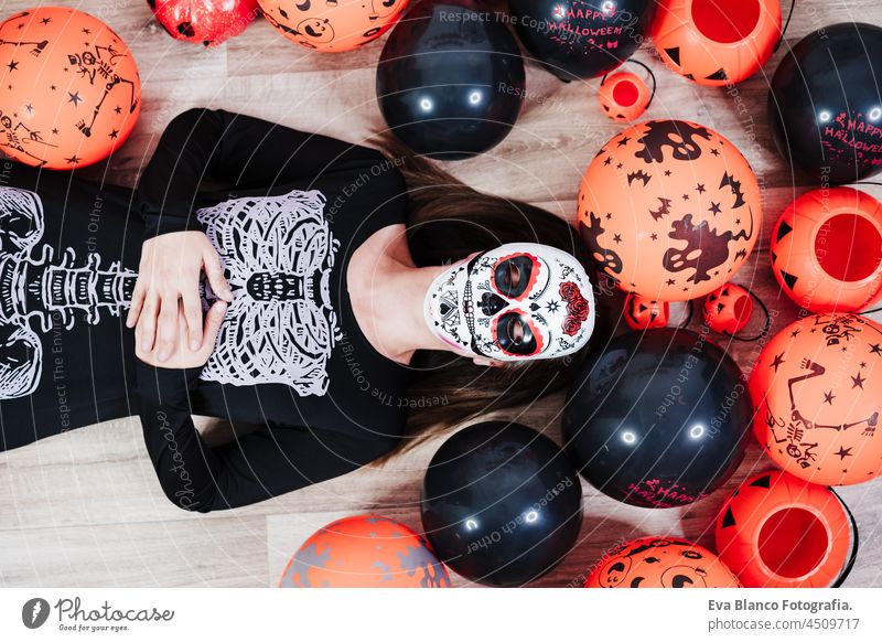 Frau trägt mexikanische Gesichtsmaske während Halloween-Feier. Frau mit geschlossenen Augen trägt Skelett-Kostüm und liegt auf dem Boden vorgibt, tot zu sein. Halloween-Party-Konzept