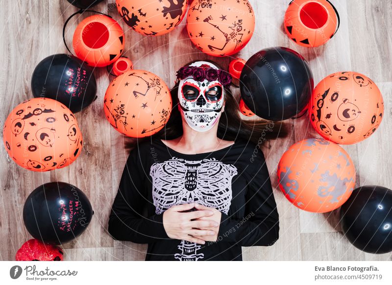 Frau trägt mexikanische Gesichtsmaske während Halloween-Feier. Frau mit geschlossenen Augen trägt Skelett-Kostüm und liegt auf dem Boden vorgibt, tot zu sein. Halloween-Party-Konzept