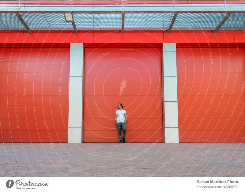 Männerporträt, das sich an eine rote Lagerhaustür lehnt Tür Fabrik sehr wenige Minimalismus Architektur Gebäude Wand industriell Garage Vorderansicht Eingang