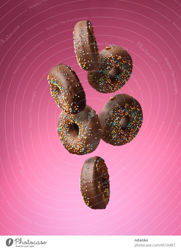 Schokolade runde Donuts mit bunten Zuckerstreuseln schweben auf einem rosa Hintergrund Krapfen Doughnut Lebensmittel süß Fliege verglast Bäckerei Dessert Gebäck