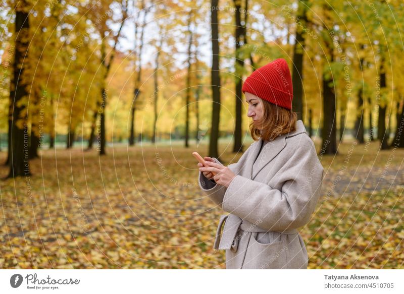 Frau benutzt ihr Telefon im Herbstpark Person benutzend Lifestyle Nachricht Internet Mitteilung Mobile Smartphone jung Technik & Technologie im Freien