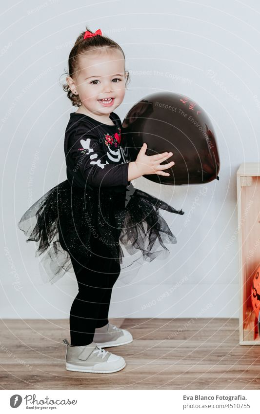 lächelnd schöne einjährige kaukasische Mädchen in Halloween-Kostüm zu Hause mit Halloween-Dekoration, hält Ballon. Lebensstil in Innenräumen. Halloween-Party-Konzept.