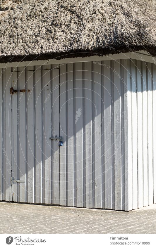 Reetgedeckter Holzschuppen Reetdach Licht Schatten Abstellraum Tür Türbeschlag Linien Dänemark Ferienhaus Pflastersteine Außenaufnahme Menschenleer grau beige