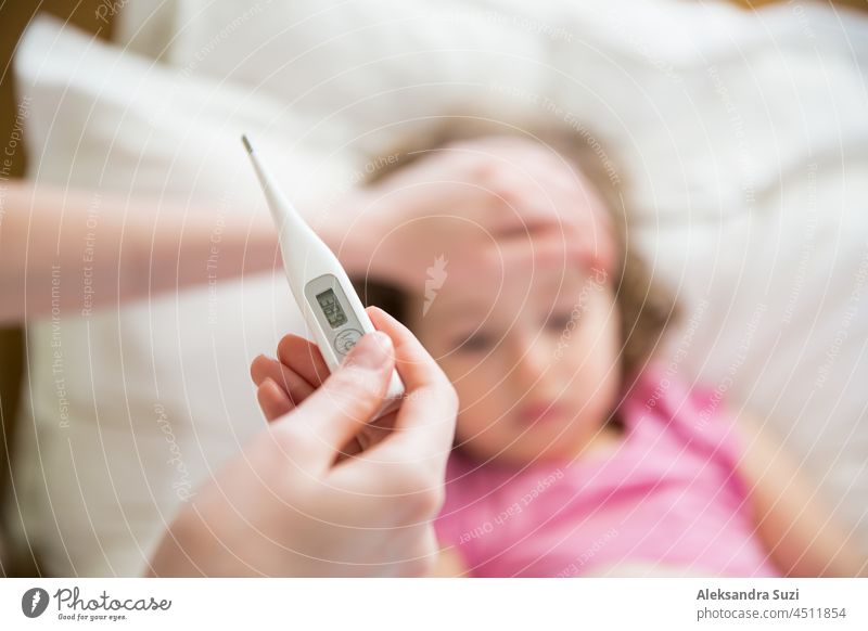 Nahbereichsthermometer. Mutter misst die Temperatur ihres kranken Kindes. Krankes Kind mit hohem Fieber im Bett liegend und Mutter hält Thermometer. Hand auf der Stirn.