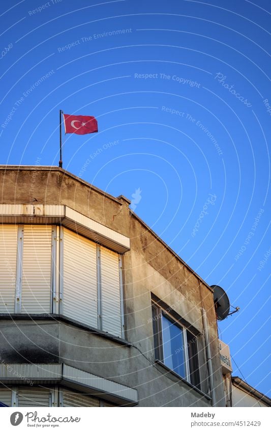 Alte Fassade eines Eckhaus mit heruntergelassenen Jalousien und oder türkischer Fahne vor blauem Himmel im Licht der Abendsonne in Foca am Ägäischen Meer in der Provinz Izmir in der Türkei
