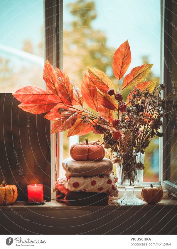 Gemütliche Herbst Stillleben mit Kerze, Pullover, Kürbis und Herbst Zweige auf Fensterbank Hintergrund. Hygge Lebensstil zu Hause mit warmer Kleidung und gemütliche Dekoration. Vorderansicht.