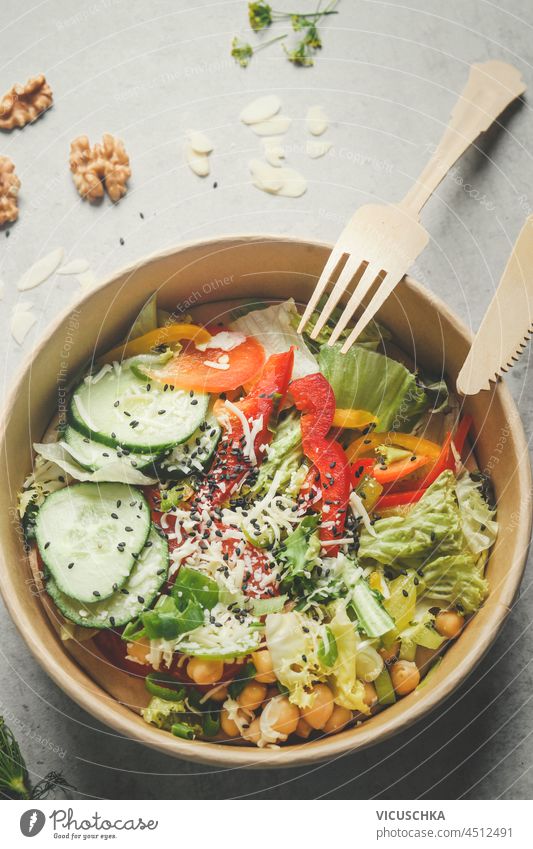 Bunter Salat mit Gemüse in plastikfreiem Lebensmittelbehälter: Gurke, Paprika, Salat, Kichererbsen und Nüsse. Nachhaltiger Lebensstil mit gesunder veganer Ernährung. Ansicht von oben.
