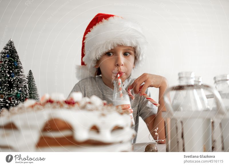 Guten Weihnachtsmorgen. Ein blonder Junge mit einer roten Weihnachtsmannmütze frühstückt, trinkt Milch melken trinken Lebensmittel süß weiß Weihnachten