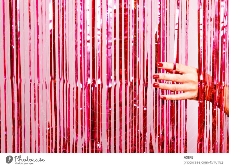 Schöne Frau Hand mit Nagellack in rot brechen durch eine rosa Lametta Party Gardine Schönheit Mode Folie Glitter Neujahr schimmern retro glühen Glanz